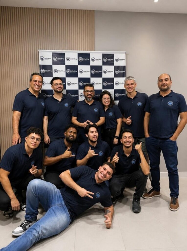 Equipe InforWay reunida em frente ao painel da empresa